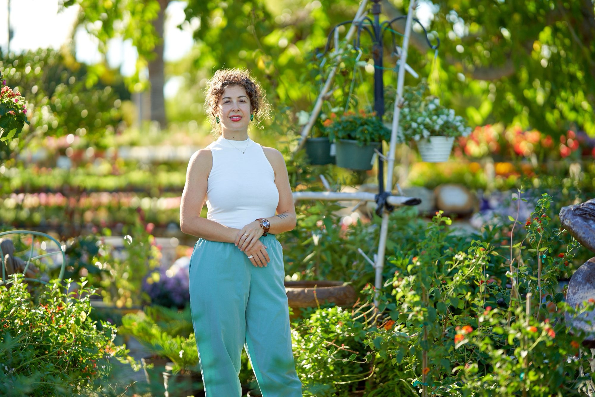 Caitlin standing in a sunlit garden surrounded by flowering plants